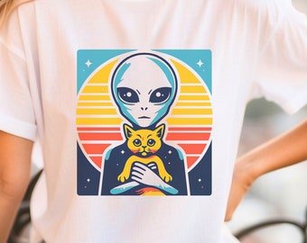 Może przedstawiać: Biała koszulka z grafiką w stylu retro przedstawiającą szarego kosmitę trzymającego żółtego kota. Grafika umieszczona jest na kolorowym tle z zachodem słońca i gwiazdami.