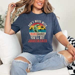 Puede incluir: Una camiseta azul marino con un gráfico de estilo vintage de un dinosaurio con palmeras y el texto "Don't mess with Mama-saurus you'll get Jurasskicked".