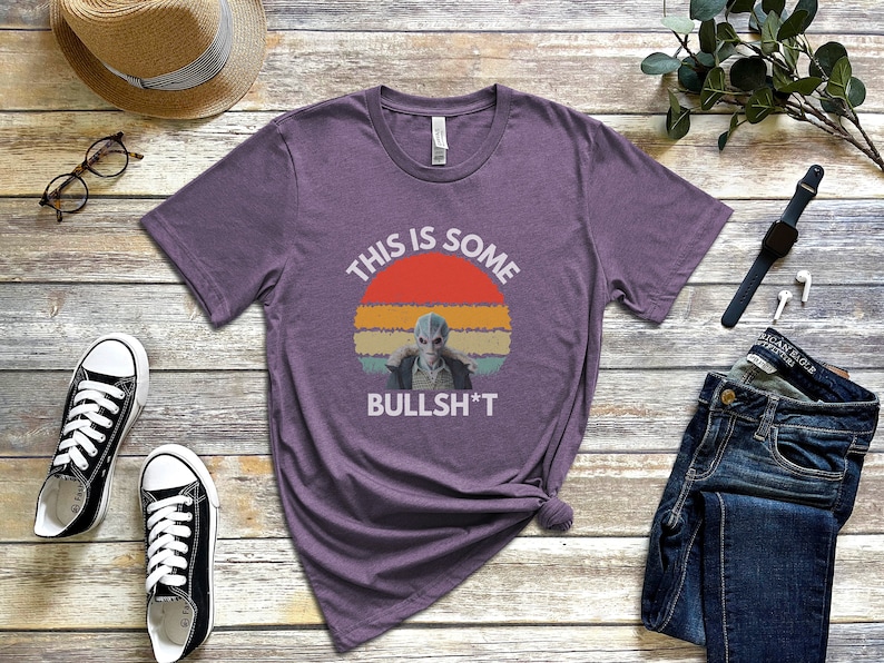 May include: Purple t-shirt with a retro sunset graphic and the text "This is some bullsh*t". The graphic features a blue alien character.
