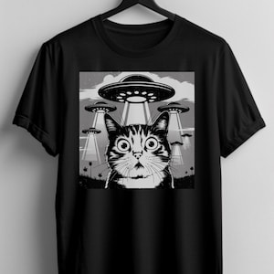 Puede incluir: Camiseta negra con un gr&aacute;fico en blanco y negro de un gato sorprendido mirando ovnis. El gato tiene ojos grandes y el dise&ntilde;o incluye platillos volantes y un cielo nublado. Un dise&ntilde;o humor&iacute;stico para los amantes de los gatos y la ciencia ficci&oacute;n.