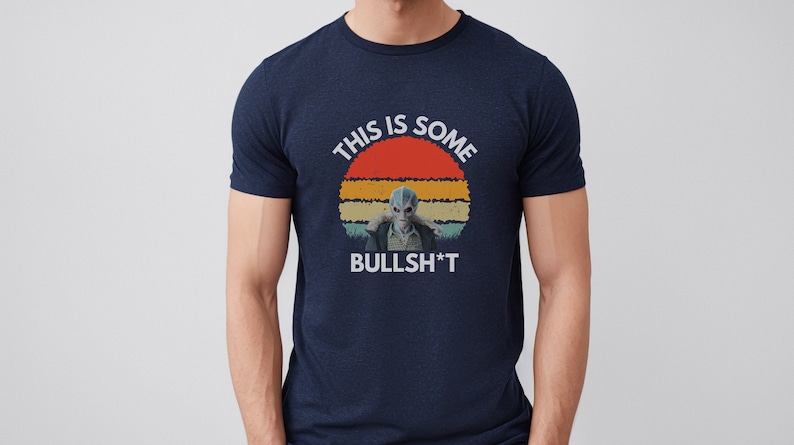 May include: A navy blue t-shirt with a retro sunset graphic and the text "This is some BULLSH*T". The graphic features a blue alien character.