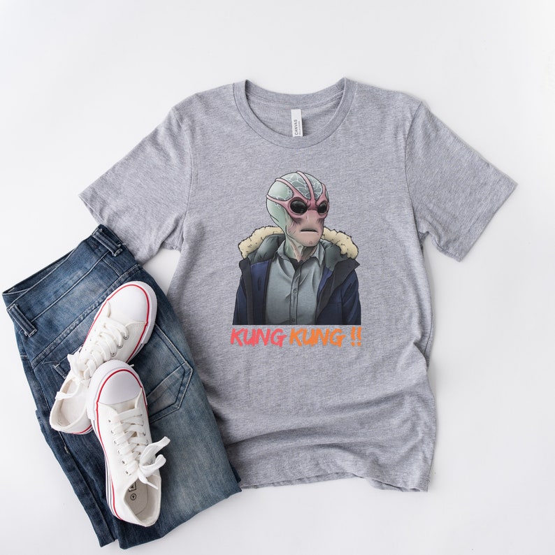 May include: A grey t-shirt with a graphic of a pink and green alien wearing a blue jacket and the text "Kung Kung!!" printed in orange and red.