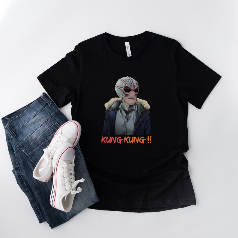 May include: Black t-shirt with a graphic of a creature with a pink and grey face wearing a blue jacket and the text "KUNG KUNG!!" in red.