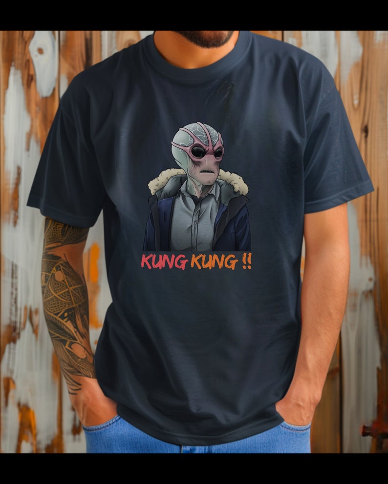 May include: A dark blue t-shirt with a graphic print of a gray alien wearing a winter coat and sunglasses. The text "KUNG KUNG!!" is printed in orange and red below the alien.
