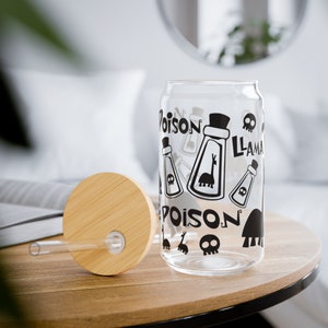 Op de afbeelding: Een transparante glazen kan met een zwart-wit ontwerp met de woorden "Poison" en "Llama" en een cartoon afbeelding van een lama. De kan heeft een bamboe deksel met een rietje.