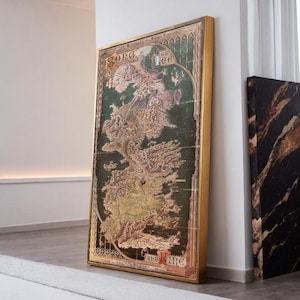 May include: A framed map print with a gold-colored frame. The map depicts a detailed geographical layout with green and brown tones. The text "Song of Ice and Fire" is visible at the top and "And Ire" at the bottom.