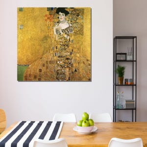 May include: A framed print of Gustav Klimt's "Portrait of Adele Bloch-Bauer I." The artwork features a woman in a gold dress against a gold background. The painting has intricate patterns and details, with a black hat and a high collar.