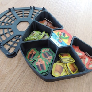 May include: Black plastic game organizer with six compartments. Each compartment contains different colored game pieces, including red, yellow, green, and brown.