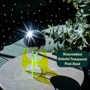 May include: A small disco ball sits on a neon green, transparent Plexi stand. The stand casts a shadow on the grey surface. The text on the image reads: Disassembled Colorful Transparent Plexi Stand.