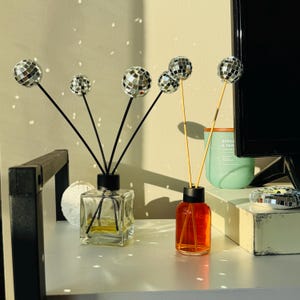 May include: Two glass diffuser bottles with disco ball accents. One bottle is square and clear, the other is round and orange. Both have black tops and black reeds. A green candle and a small disco ball are also visible.