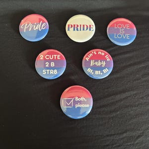 May include: Five circular pinback buttons featuring bisexual pride flag colors of pink, purple, and blue. Text includes: Pride, PRIDE, LOVE IS LOVE, 2 CUTE 2 B STR8, Ain't no lie Baby BI, BI, BI, and a checkbox with the text Both, please.