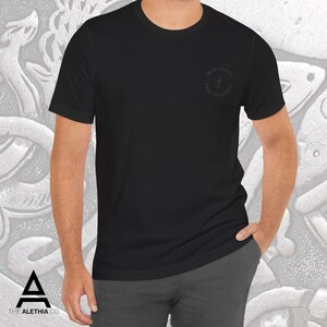 May include: Black crew neck t-shirt with the text "SEEK GLORY FEAR NOTHING" in a circular design on the upper left chest. The shirt is a solid black color and is made of a soft material. The Alethia Co. logo is visible in the bottom left corner.