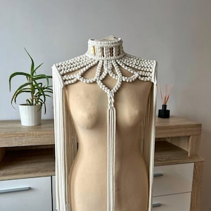 May include: A white macrame choker necklace with long fringe. The necklace is made of cotton cord and has a gold metal accent.