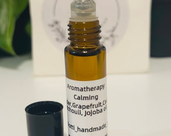 Op de afbeelding: Amberkleurige glazen aromatherapie roll-on fles met een doorzichtige rollerball top en een zwarte dop. De fles heeft een wit etiket met de woorden "Aromatherapie Kalmerend" en de ingrediënten. De fles is ongeveer 7,6 cm hoog.
