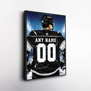 May include: Framed artwork featuring a hockey player in a black jersey with the text "ANY NAME" and the number "00". The player is wearing a black helmet with the word "KINGS". The background has blue and white lighting.