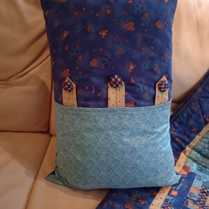 May include: A blue and green pillow with a heart pattern and three buttons. The pillow has a pocket on the back.