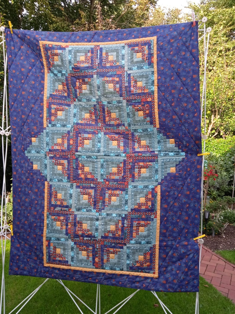 May include: A blue and orange quilt with a log cabin pattern. The quilt is hanging on a clothesline.