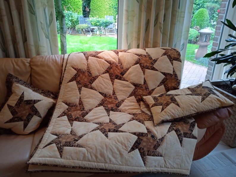 May include: A beige and brown patchwork quilt with a star pattern. The quilt is on a couch with two matching pillows.