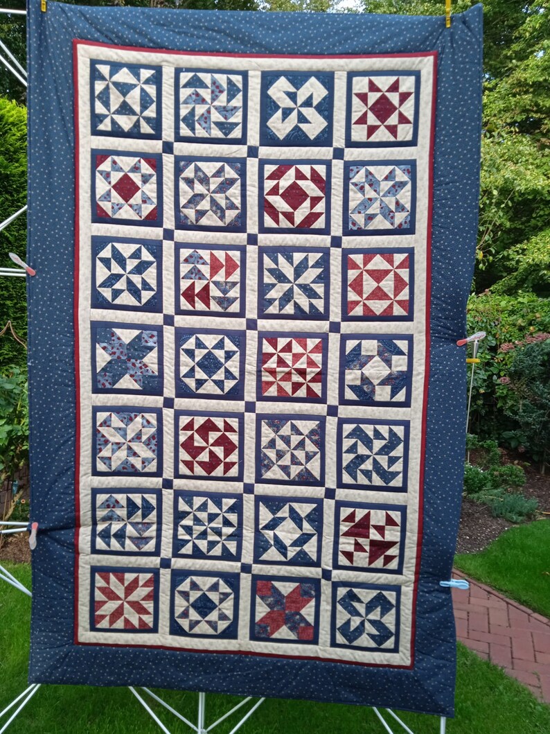 May include: A blue and white quilt with a patchwork design featuring various geometric shapes. The quilt is made up of 36 individual squares, each with a different pattern. The quilt is hanging on a clothesline.