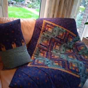 May include: A blue and green patchwork quilt with a geometric pattern. The quilt is folded and placed on a brown leather couch with a blue and green pillow.