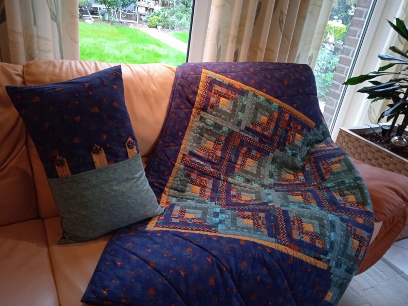 May include: A blue and green patchwork quilt with a geometric pattern. The quilt is folded and placed on a brown leather couch with a blue and green pillow.