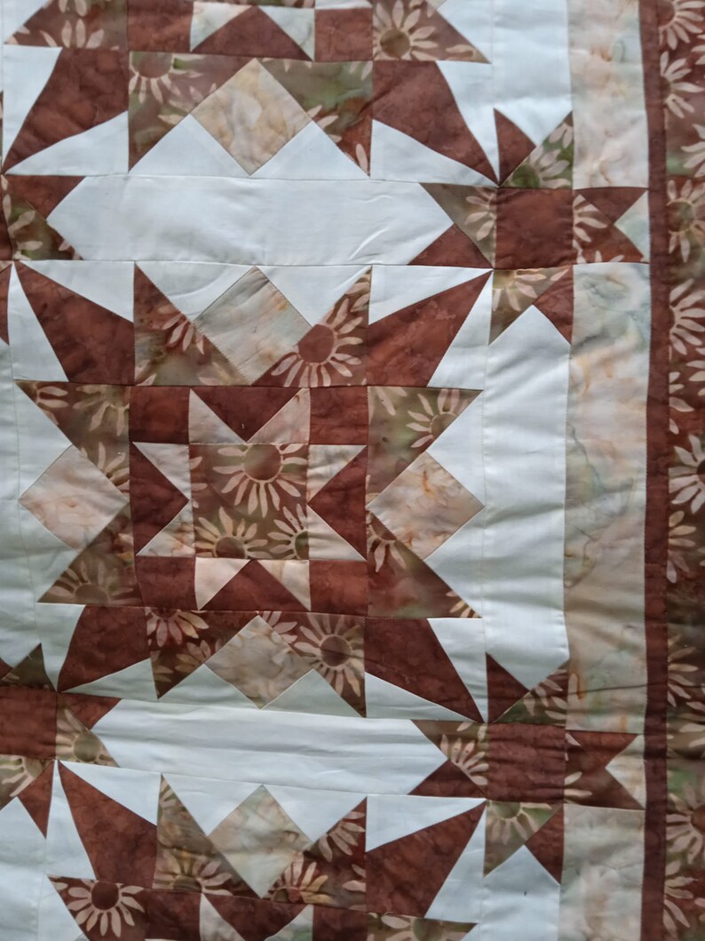 Puede incluir: Una colcha con un patr&oacute;n geom&eacute;trico marr&oacute;n y blanco. La colcha est&aacute; hecha de tela con estampado floral.