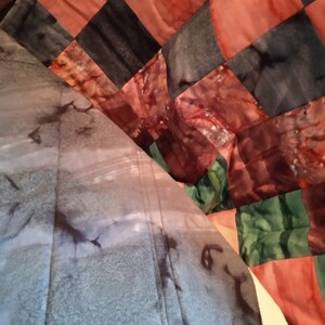 Pode incluir: Uma colcha com um design de patchwork que apresenta quadrados de diferentes cores e padr&otilde;es. A colcha &eacute; feita de tecido com efeito tie-dye. As cores incluem tons de marrom, laranja, verde e azul.