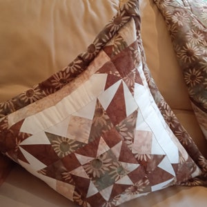 Puede incluir: Dos almohadas decorativas con un patr&oacute;n floral marr&oacute;n, blanco y beige. Las almohadas est&aacute;n hechas de tela y tienen una forma cuadrada.