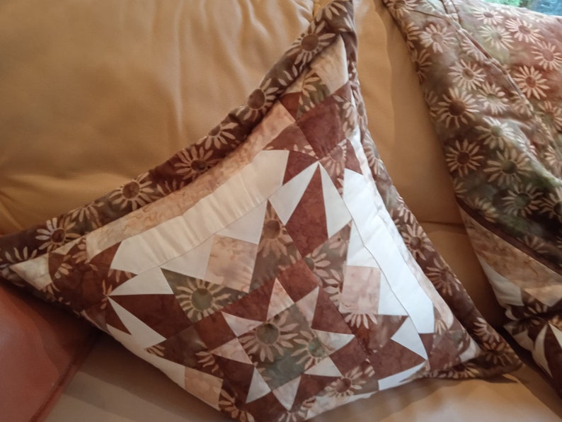 Puede incluir: Dos almohadas decorativas con un patr&oacute;n floral marr&oacute;n, blanco y beige. Las almohadas est&aacute;n hechas de tela y tienen una forma cuadrada.