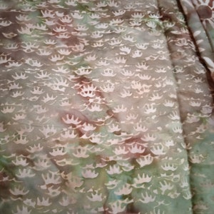 Puede incluir: Primer plano de una tela con un patr&oacute;n de te&ntilde;ido anudado verde, marr&oacute;n y blanco. La tela tiene un patr&oacute;n repetitivo de coronas blancas.