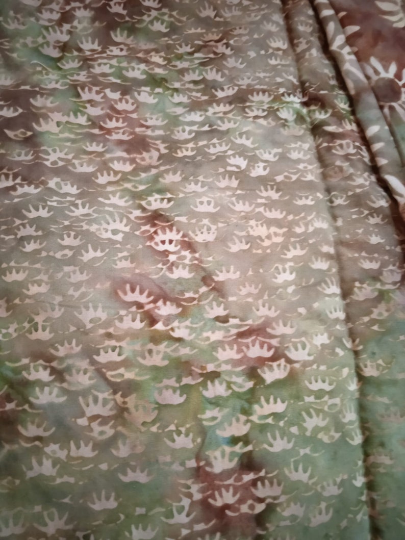 Puede incluir: Primer plano de una tela con un patr&oacute;n de te&ntilde;ido anudado verde, marr&oacute;n y blanco. La tela tiene un patr&oacute;n repetitivo de coronas blancas.