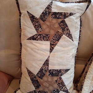May include: Two beige throw pillows with a brown and white star pattern. The pillows have a white background with a brown star pattern and a white border.
