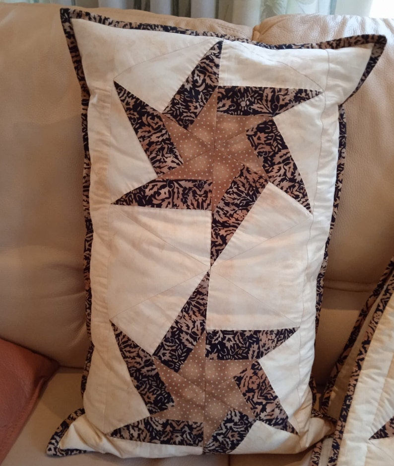 May include: Two beige throw pillows with a brown and white star pattern. The pillows have a white background with a brown star pattern and a white border.