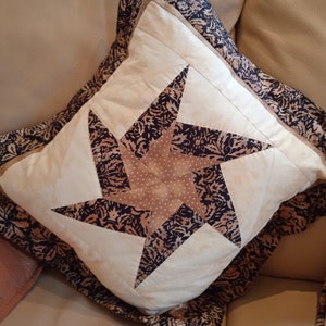 May include: A decorative pillow with a brown and white star pattern. The pillow has a black and brown patterned border.