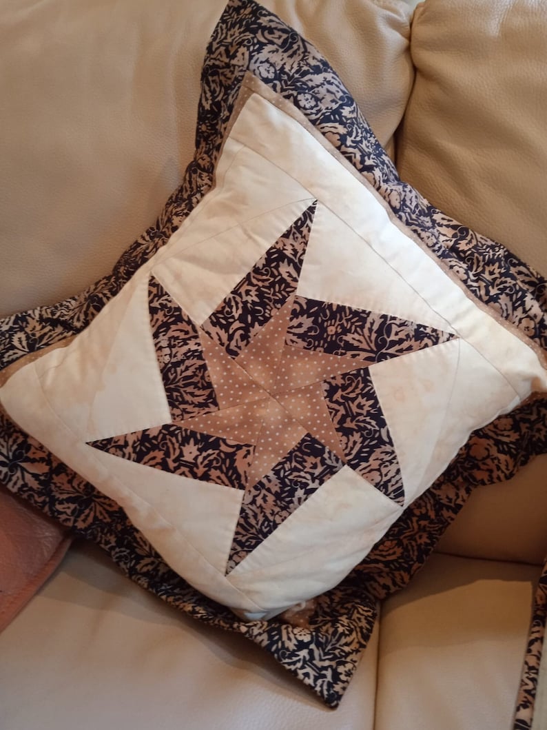 May include: A decorative pillow with a brown and white star pattern. The pillow has a black and brown patterned border.