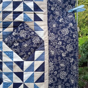 May include: A blue and white quilt with a geometric pattern of triangles. The quilt is hanging on a clothesline with clothespins.