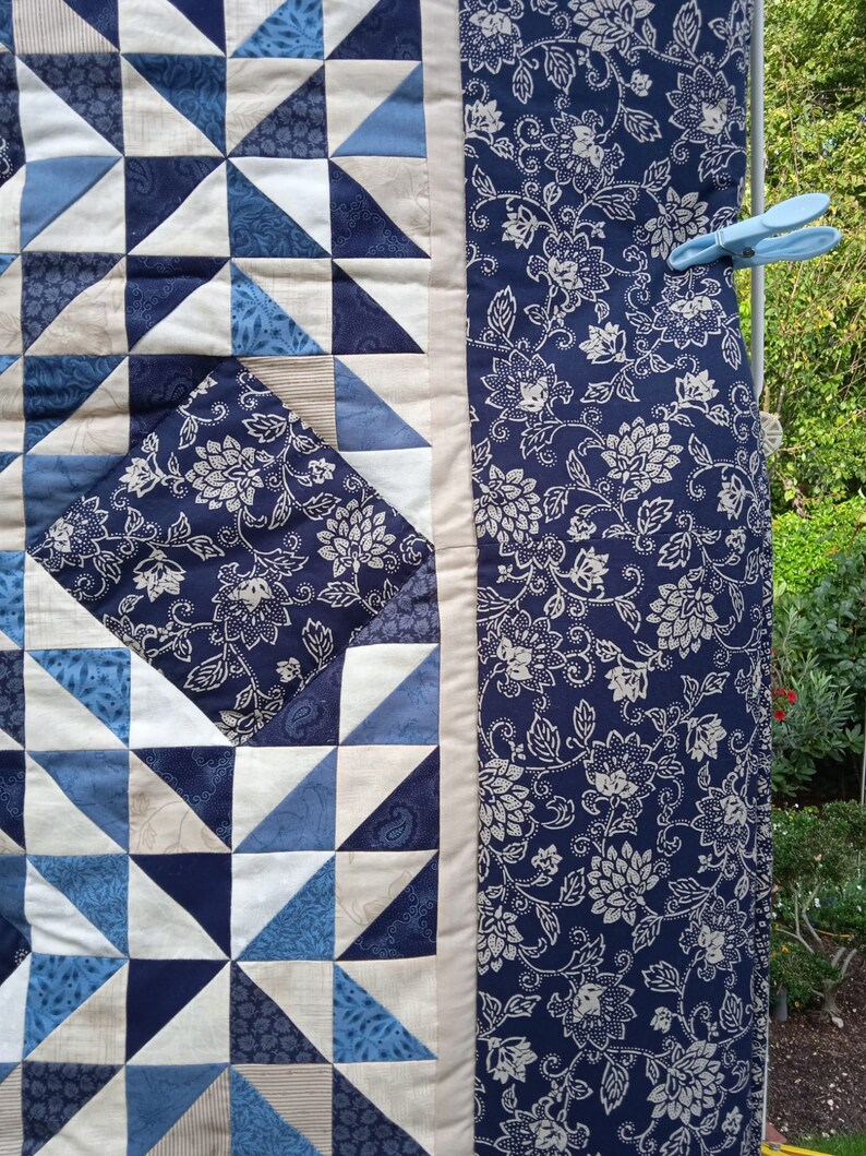 May include: A blue and white quilt with a geometric pattern of triangles. The quilt is hanging on a clothesline with clothespins.