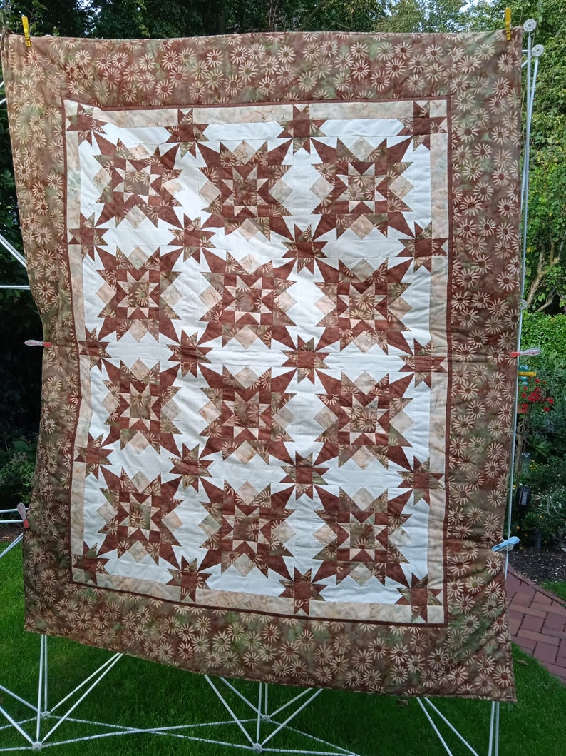 Puede incluir: Una colcha marr&oacute;n y blanca con un patr&oacute;n de estrella. La colcha est&aacute; hecha de tela con estampado floral y est&aacute; colgada de un tendedero.