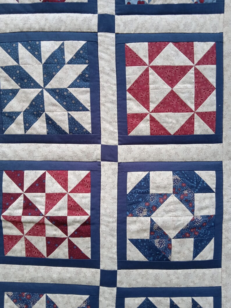 May include: A quilt with a patchwork design featuring red, white and blue squares. Each square has a different pattern of triangles.