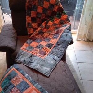 Pode incluir: Uma poltrona marrom com uma colcha de patchwork feita de tecido laranja, verde e cinza. A colcha est&aacute; dobrada sobre o encosto da poltrona e drapeada sobre o assento.