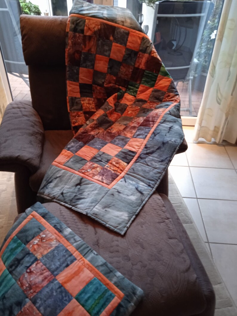 Pode incluir: Uma poltrona marrom com uma colcha de patchwork feita de tecido laranja, verde e cinza. A colcha est&aacute; dobrada sobre o encosto da poltrona e drapeada sobre o assento.