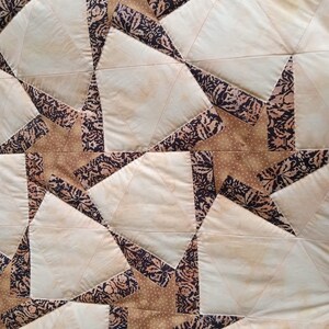 May include: A quilt made of fabric squares in shades of brown, beige, and white. The squares are sewn together to create a pattern of stars. The fabric has a floral print.