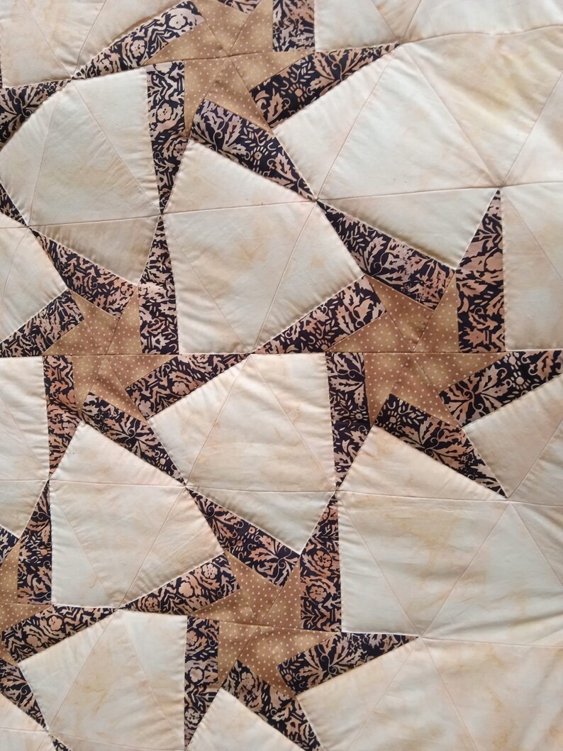 May include: A quilt made of fabric squares in shades of brown, beige, and white. The squares are sewn together to create a pattern of stars. The fabric has a floral print.
