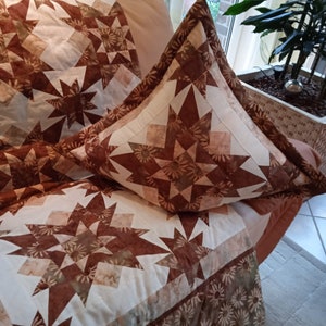 Puede incluir: Una colcha marr&oacute;n y crema con un patr&oacute;n de estrella. La colcha est&aacute; hecha de tela con estampado floral. La colcha est&aacute; en un sof&aacute; con una almohada a juego.