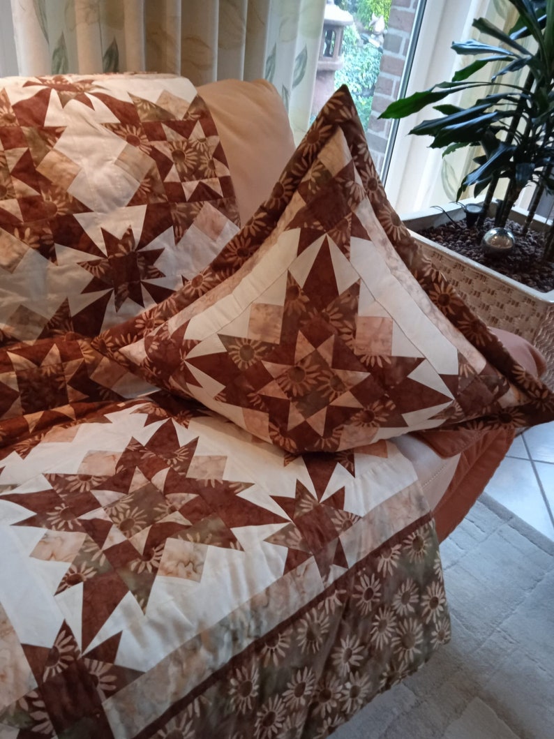 Puede incluir: Una colcha marr&oacute;n y crema con un patr&oacute;n de estrella. La colcha est&aacute; hecha de tela con estampado floral. La colcha est&aacute; en un sof&aacute; con una almohada a juego.