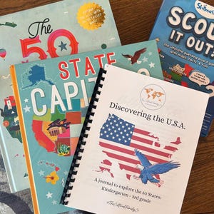 Op de afbeelding: Een spiraalgebonden notitieboek met een kleurrijke illustratie van de kaart van de Verenigde Staten en een adelaar. De omslag heeft de tekst "Discovering the U.S.A. A journal to explore the 50 States: Kindergarten - 3rd grade".