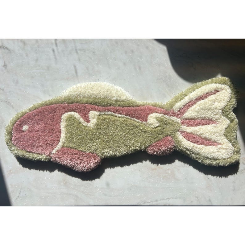 May include: A pink and green fish-shaped rug with a white outline. The rug is made of a soft, fluffy material.