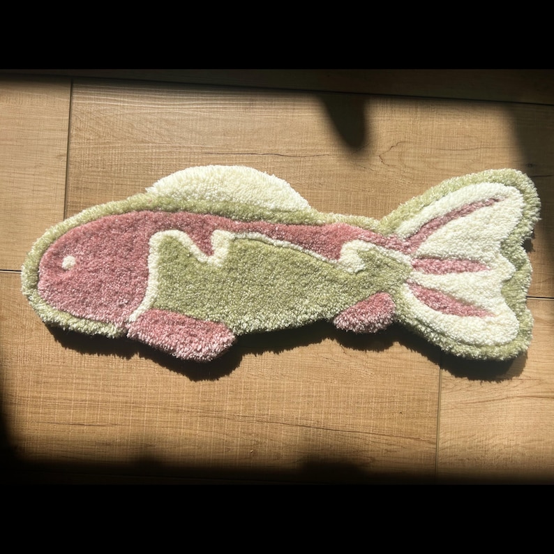 May include: A green and pink fish-shaped rug with a fluffy texture. The rug is made of a soft, plush material and has a whimsical design.