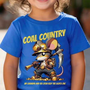 May include: A young child wearing a royal blue t-shirt with a cartoon mouse wearing a miner's hat and holding a pickaxe. The shirt says "Coal Country" and "My grandpa and his crew keep the lights on!"