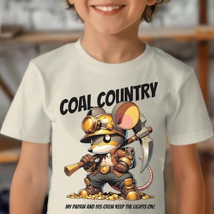 May include: A young person wearing a white t-shirt with a cartoon image of a mouse wearing a miner's hat and holding a pickaxe. The text "COAL COUNTRY" is above the image and "MY PAPAW AND HIS CREW KEEP THE LIGHTS ON!" is below the image.